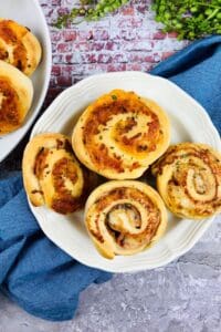 A white plate with five golden brown garnished with herbs, sits on a blue cloth atop a stone surface.