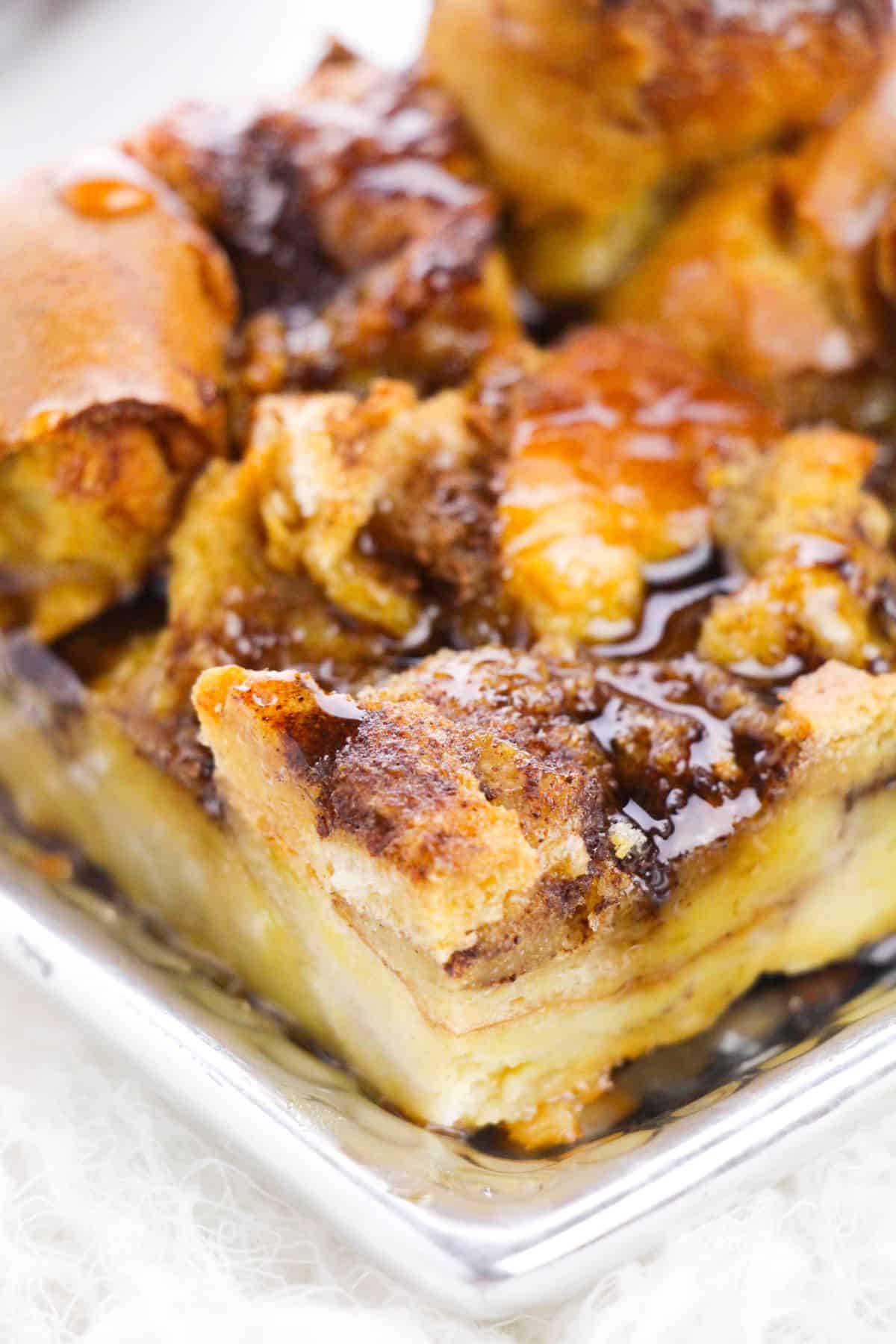 Close-up of a Brioche French Toast Casserole, baked to perfection and topped with cinnamon, then drizzled with syrup on a metal tray.