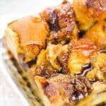 A close-up of the bread pudding, topped with cinnamon, brown sugar, and drizzled syrup on a metallic tray.