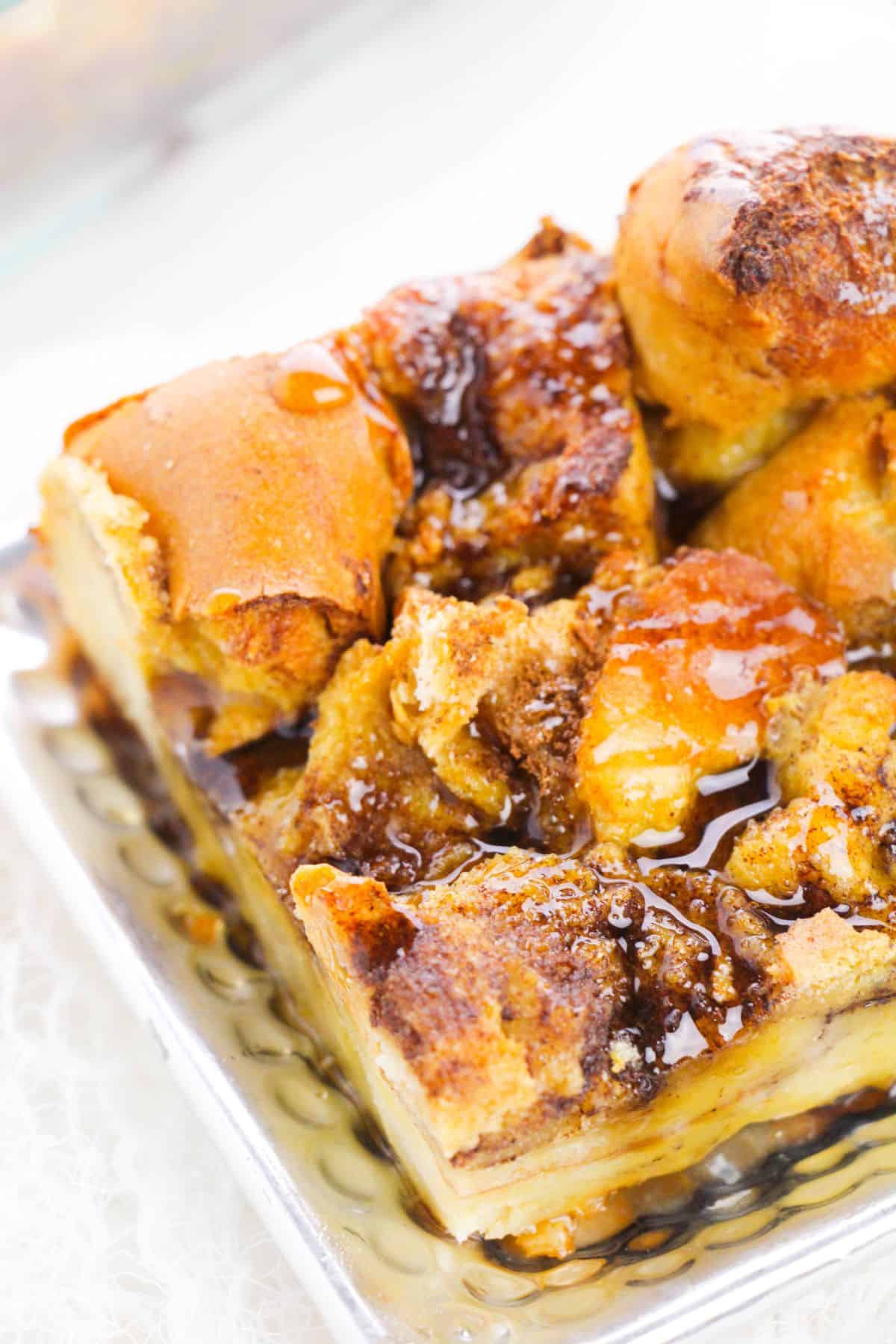 A close-up of the bread pudding, topped with cinnamon, brown sugar, and drizzled syrup on a metallic tray.
