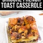 A serving of Brioche French Toast Casserole sits on a square plate, topped with syrup, with more casserole visible in the background.