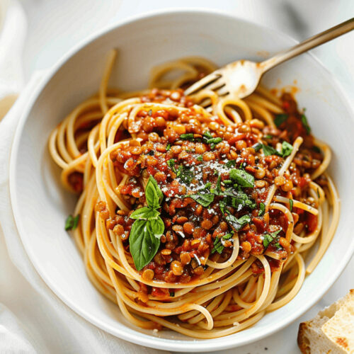 A bowl of lentils and pasta topped with tomato sauce, lentils, basil, and grated cheese, served with a side of bread.