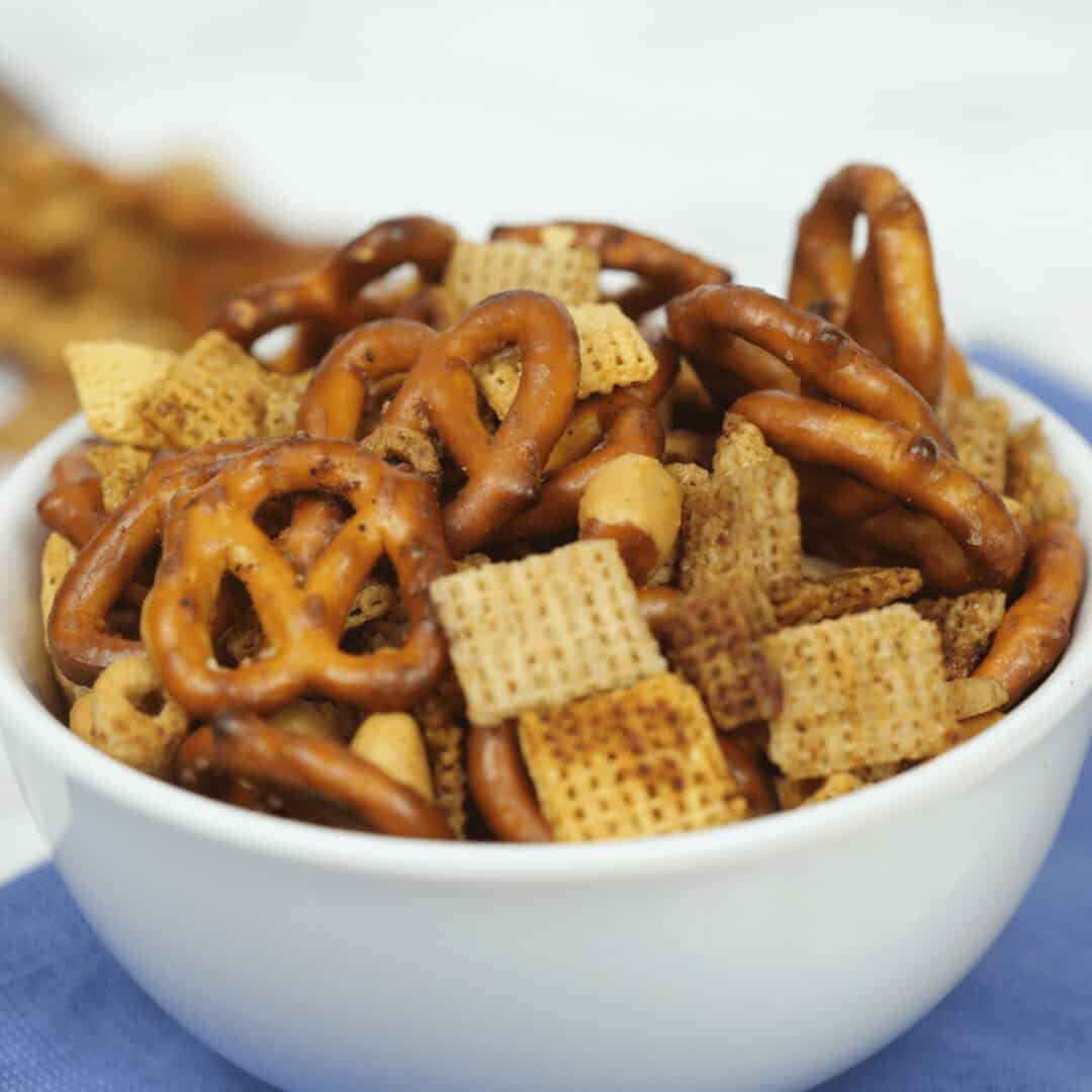 A bowl filled with a delightful Slow Cooker Chex Mix featuring pretzels, cereal squares, and peanuts.