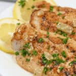 Lemon Garlic Chicken: Grilled chicken breasts topped with a zesty lemon-garlic sauce and garnished with fresh parsley, complemented by lemon slices in the background on a pristine white plate.