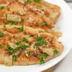 Fillets garnished with chopped parsley and cooked onions, served on a white plate.