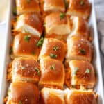 A tray filled with neatly arranged buffalo chicken sliders, topped with fresh parsley.