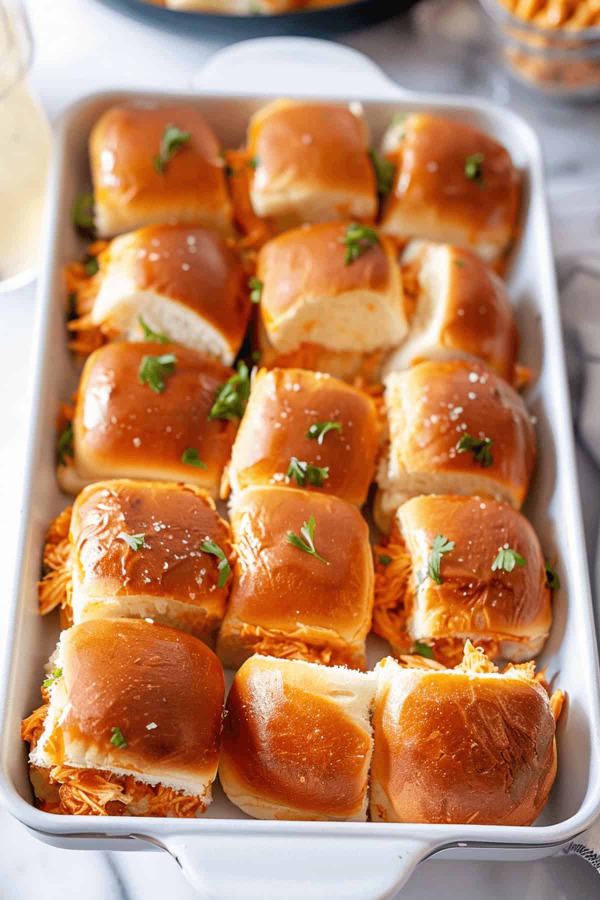 A tray filled with neatly arranged buffalo chicken sliders, topped with fresh parsley.