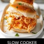 Buffalo chicken sliders rest on a white plate, garnished with a sprinkle of fresh herbs for an appealing touch.