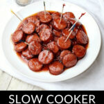 Plate of glazed cocktail sausages with toothpicks on a wooden table, labeled "Slow Cooker Cocktail Sausages.