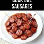 A plate of glossy slow cooker cocktail sausages with toothpicks on a wooden table.