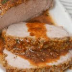 Close-up of meat slow-cooked in a crock pot, covered in a savory sauce on a white platter.
