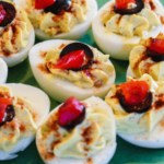 Plate of deviled eggs without mayo, garnished with paprika and olives.