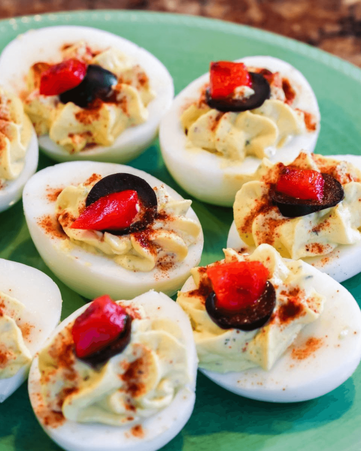 A plate of deviled eggs without mayo, garnished with paprika and a slice of olive and red pepper.