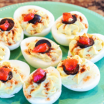 A plate of deviled eggs without mayo, garnished with paprika and olives.