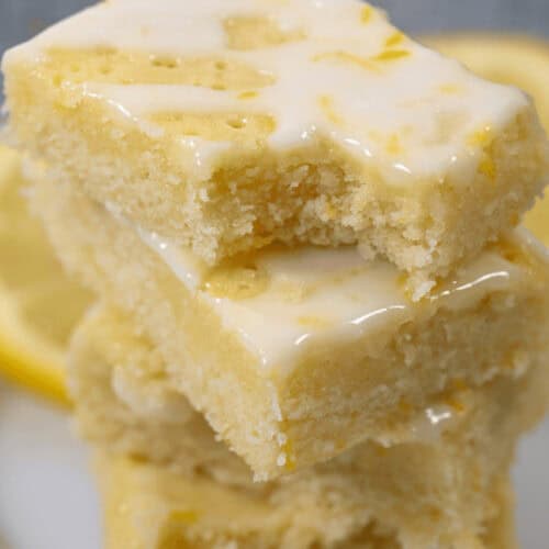 A stack of three glazed lemon brownies is artfully placed on a pristine white plate.