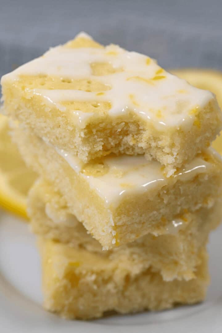 A stack of three glazed lemon brownies is artfully placed on a pristine white plate.