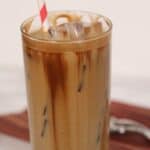 A tall glass with a red and white striped straw, filled with ice cubes, rests on a marble surface.