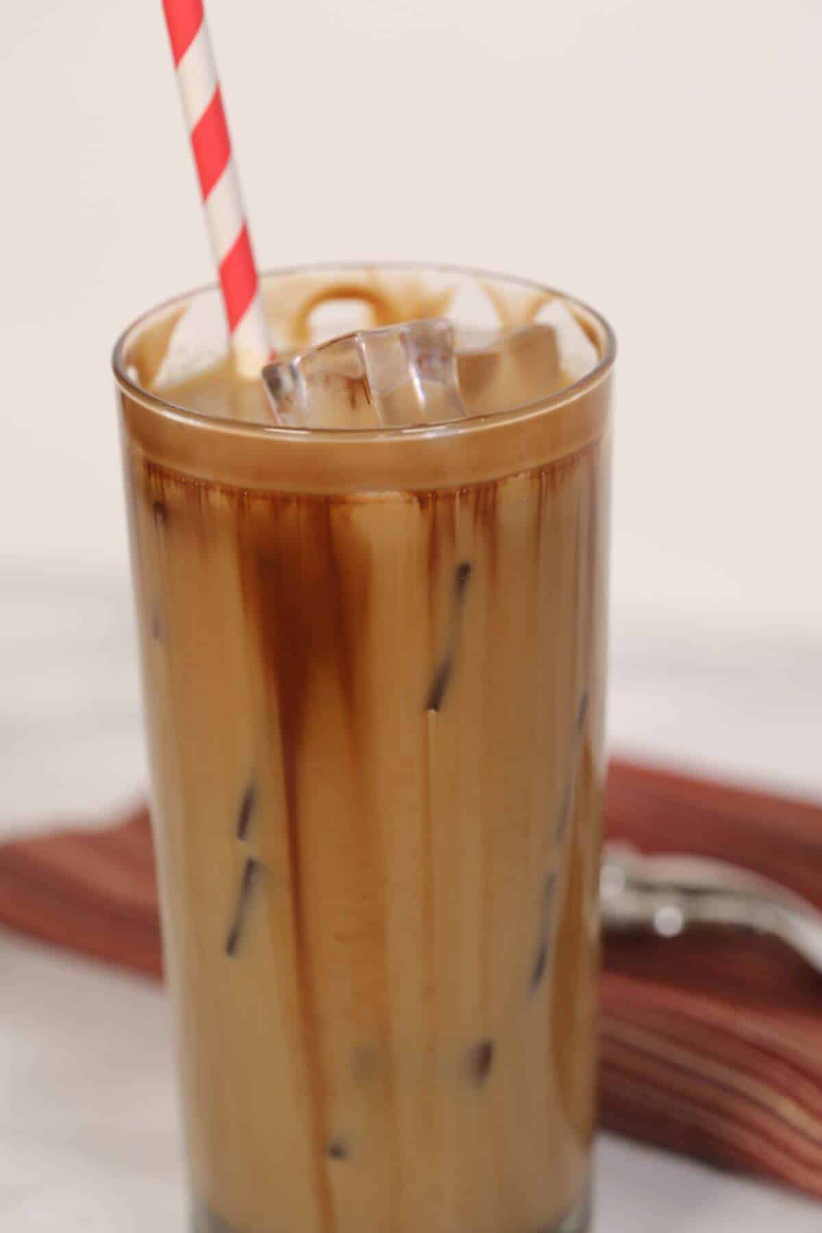 A tall glass  with a red and white striped straw, filled with ice cubes, rests on a marble surface.