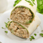 Chipotle chicken salad wrap garnished with fresh herbs on a white plate.