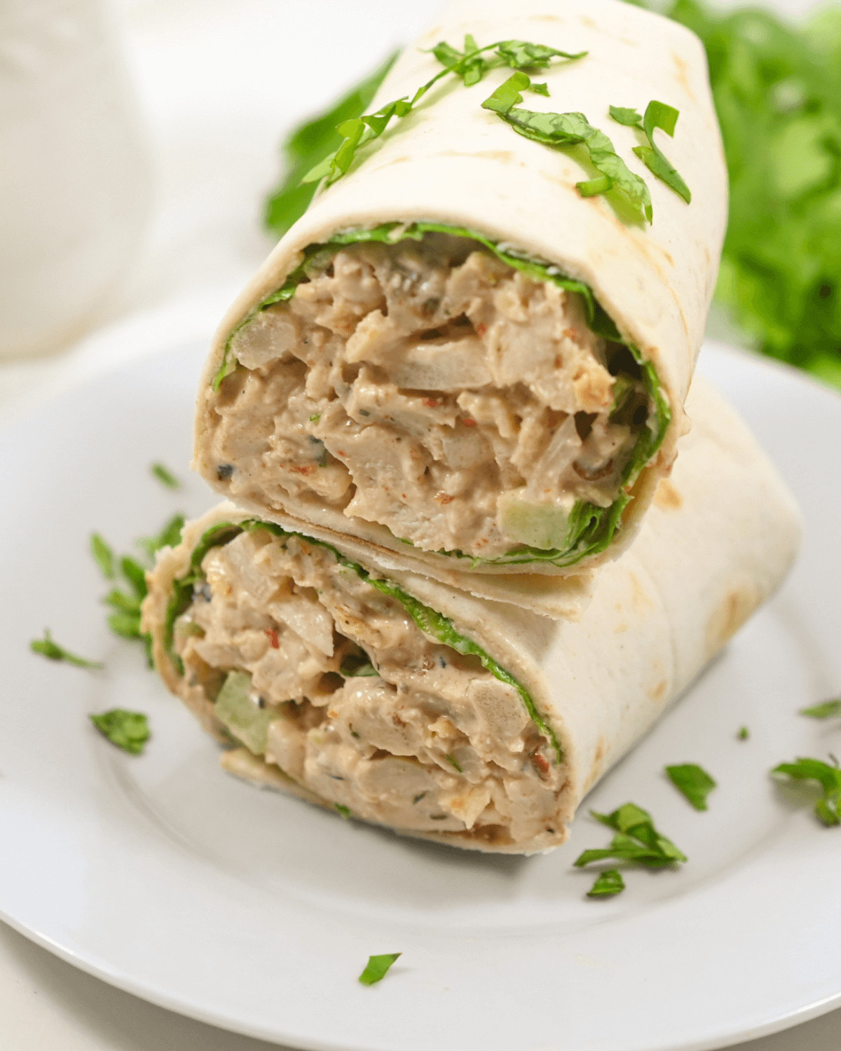 Chipotle chicken salad wrap garnished with fresh herbs on a white plate.