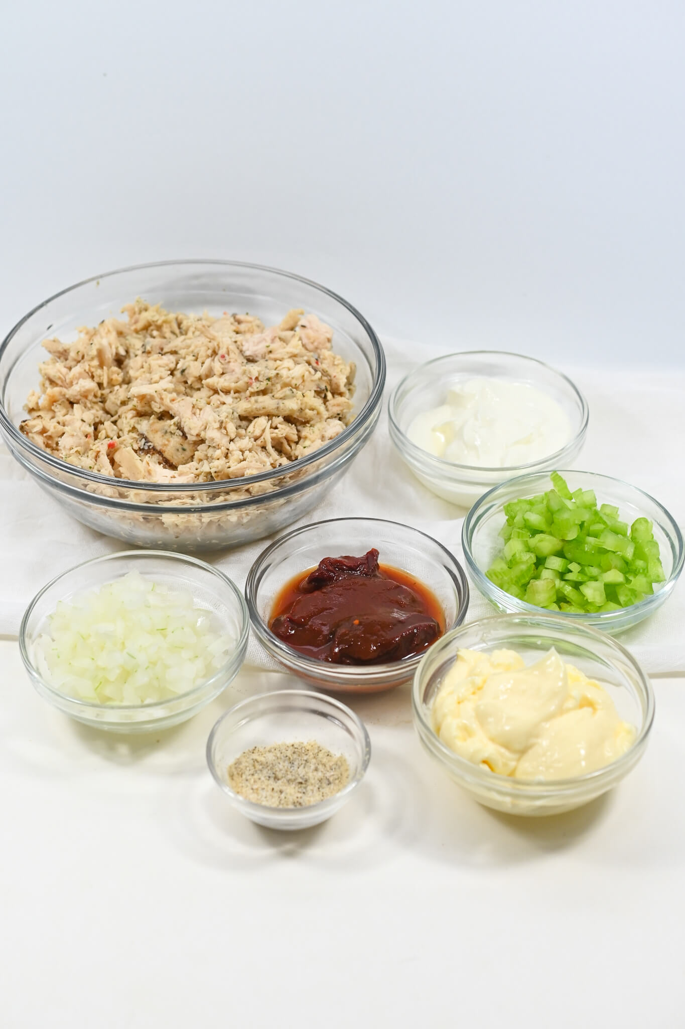 Ingredients for making a chipotle chicken salad neatly arranged in clear bowls on a white background.