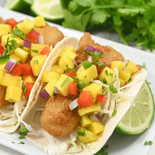 Fish tacos with mango salsa, cabbage, and lime on a white plate garnished with chipotle chicken salad.