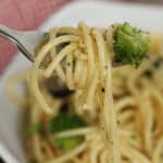 A fork holds a bite of the dish with a small piece of broccoli over a bowl of mixed greens.