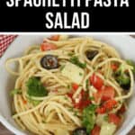 A bowl of spaghetti pasta salad with broccoli, black olives, tomato, and cucumber, garnished with herbs. The text "THE BEST SPAGHETTI PASTA SALAD" is displayed above the image. This delightful dish combines fresh vegetables with perfectly cooked spaghetti for a refreshing meal.