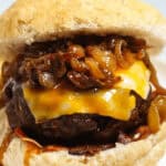 A close-up of a Whiskey Burger with melted cheese, caramelized onions, and bacon, served in a toasted bun.