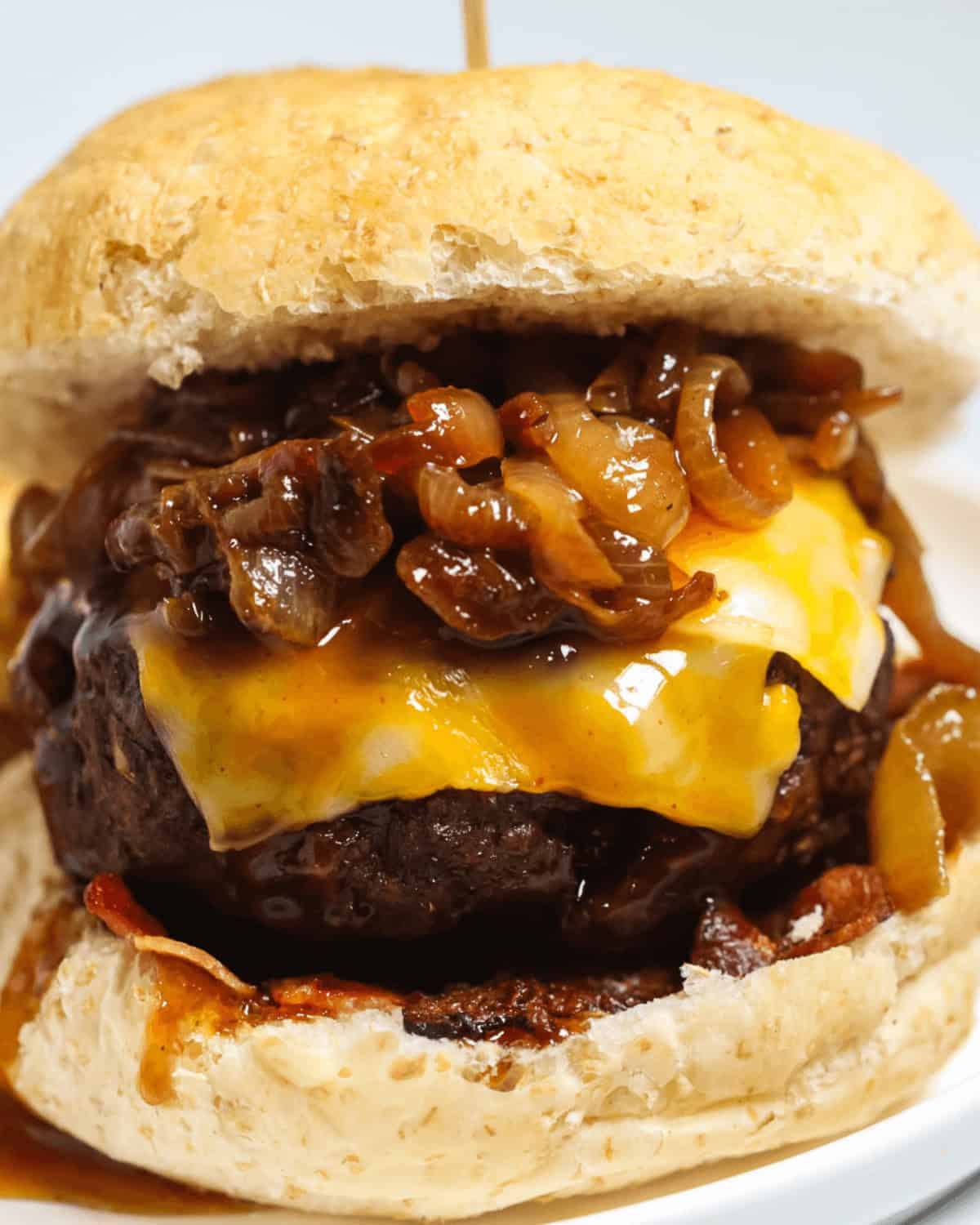 A close-up of a Whiskey Burger with melted cheese, caramelized onions, and bacon, served in a toasted bun.
