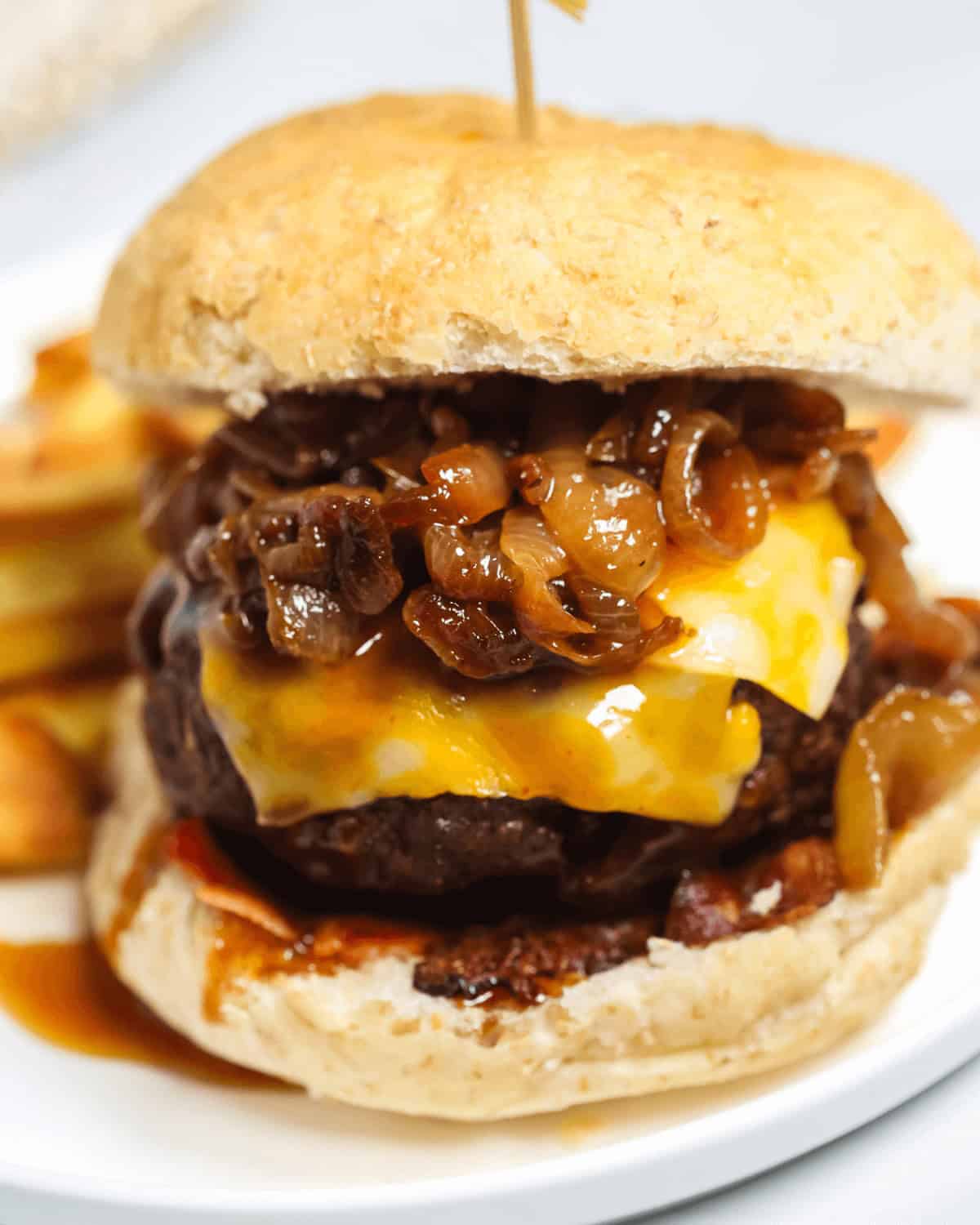 A close-up of a Whiskey Burger with caramelized onions and cheese melting over the patty, served on a white plate with a side of fries.