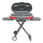 A grey and red portable grill that you can move around because of its wheels and easily collapsible.
