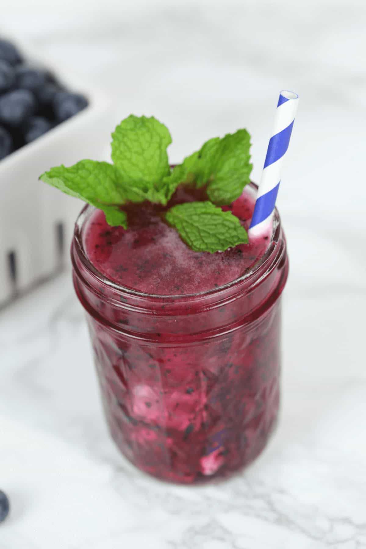 A drink topped with mints with a straw in it.