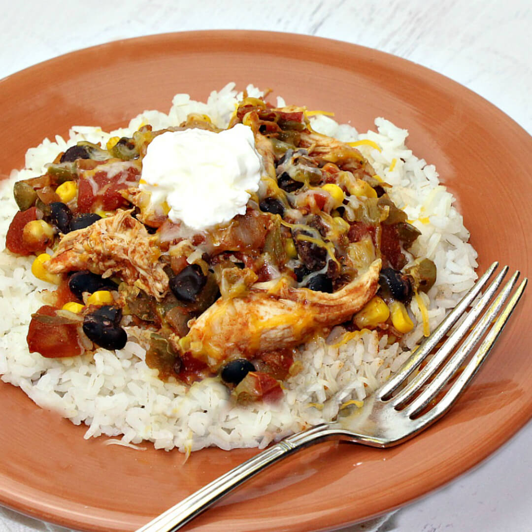 Crock Pot Tex Mex Chicken with White Rice and Sour Cream on a Orange Plate with a Metal Fork. 