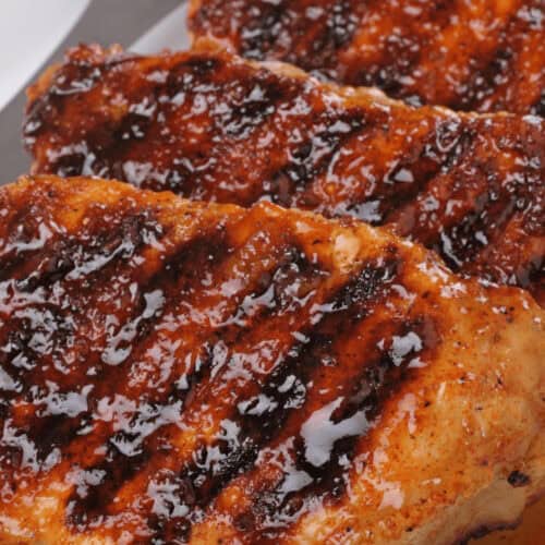 Grilled pork chops, marinated to perfection, boast a glossy, caramelized coating as they are arranged in a row on a white plate.