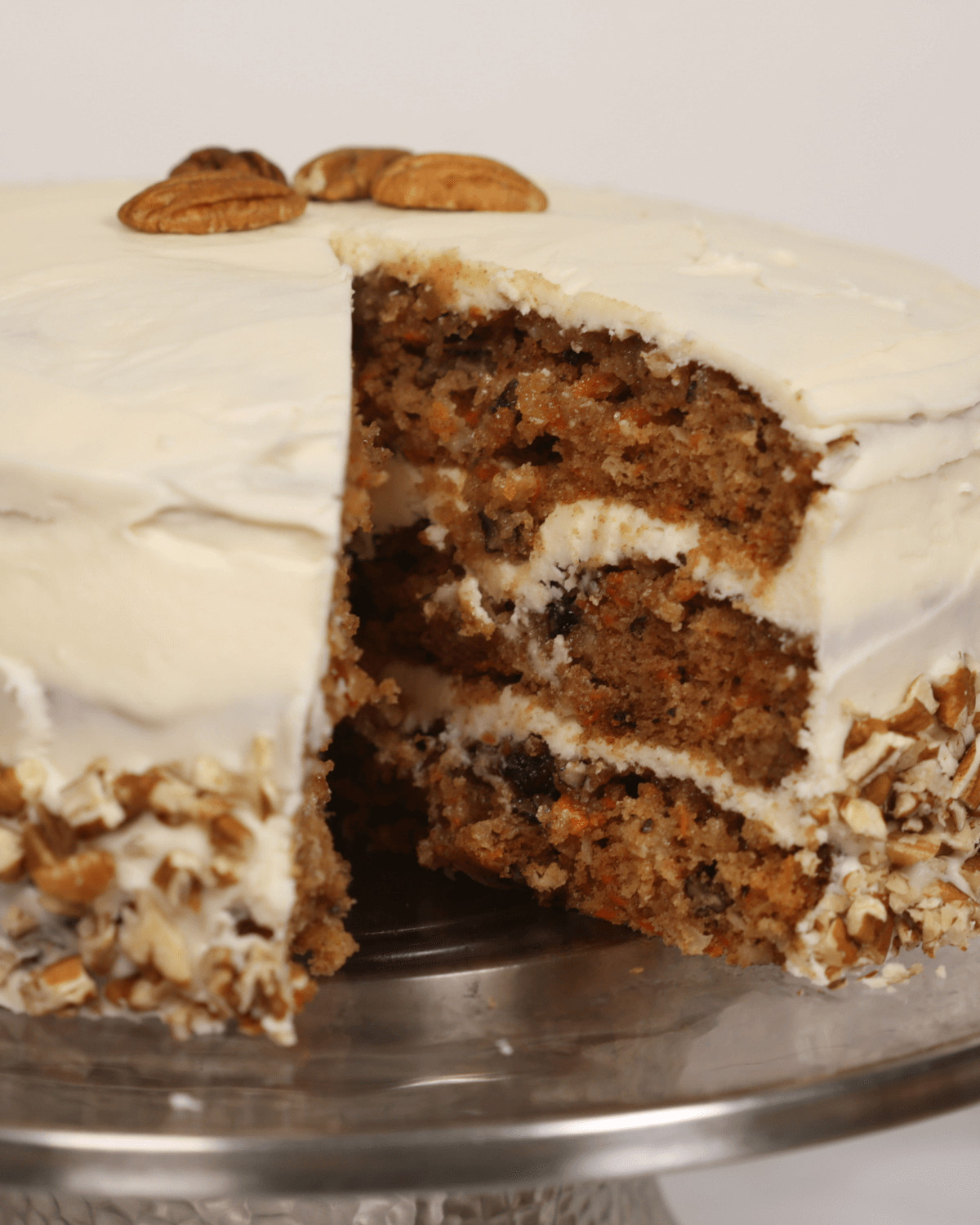 A carrot cake with pineapple and coconut, cream cheese frosting, and chopped nuts, with one slice removed.