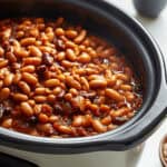 Close-up of a crock pot filled with baked beans in a rich tomato sauce.