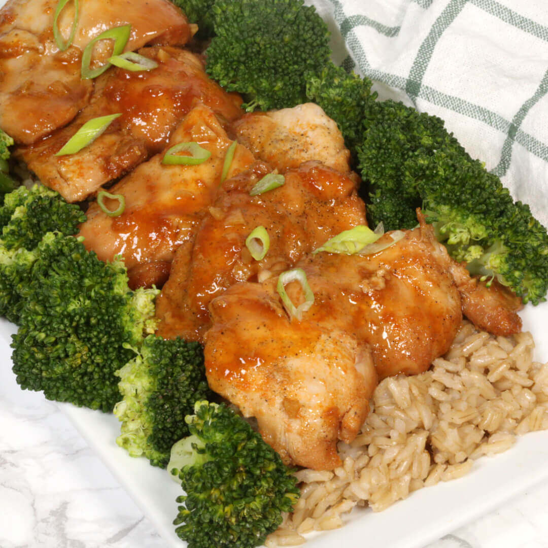 Instant Pot Pressure Cooker Honey Garlic Chicken with Broccoli and Rice on a white plate with a white and black checkered napkin.   