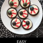 A white plate holds seven eyeball cookies, designed to resemble monster eyes with red icing veins and chocolate centers, placed on a spiderweb-patterned tablecloth. Text reads "Easy Monster Eyeball Cookies.
