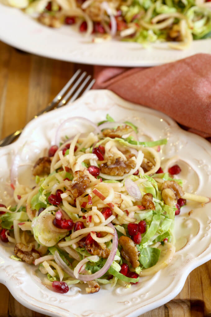 Harvest salad with layers of shaved brussels sprouts, apples, pomegranates, candied walnuts and a pomegranate vinaigrette on a white plate