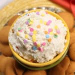 A bowl of funfetti cookie dough dip topped with colorful sprinkles, surrounded by vanilla wafer cookies.