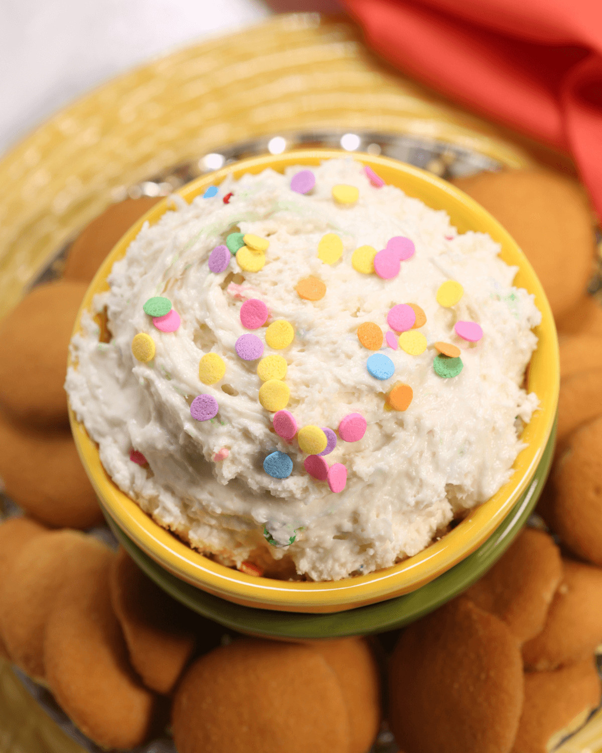 A bowl of funfetti cookie dough dip topped with colorful sprinkles, surrounded by vanilla wafer cookies.