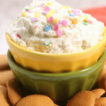 A bowl of funfetti dessert dip with sprinkles, served with cookie wafers.