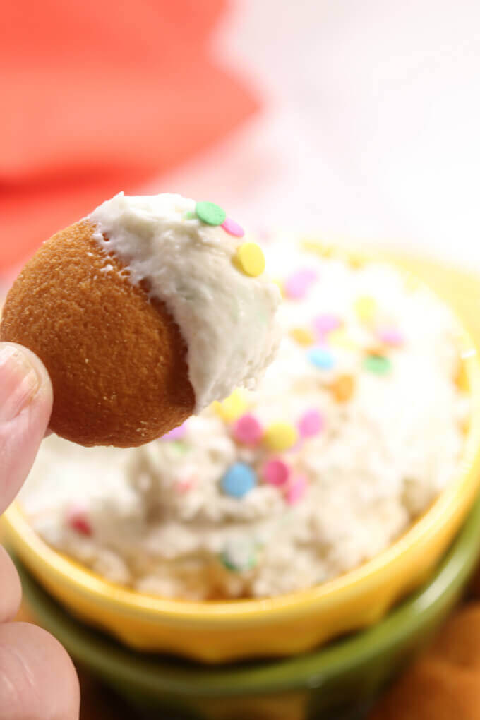 Confetti Cake Batter Dip on a cookie, with a bowl of confetti cake dip in the background. 