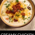 A bowl of creamy Chicken Corn Soup topped with bacon, shredded cheese, and chopped parsley, set on a light tablecloth.