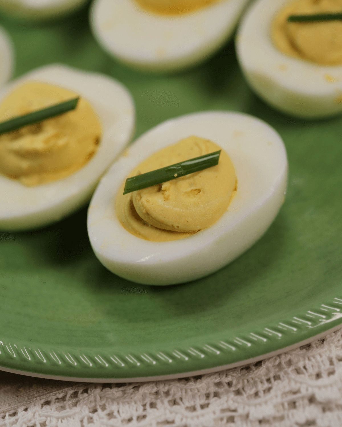 Deviled eggs without mustard, garnished with chives, served on a green plate.