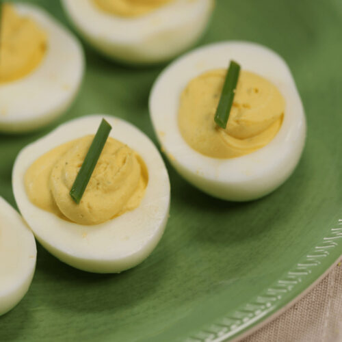 Four halves of deviled eggs without mustard, garnished with chives on a green plate.