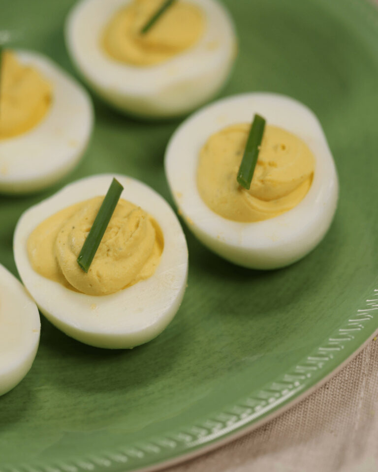 Four halves of deviled eggs without mustard, garnished with chives on a green plate.