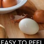 A peeled hard-boiled egg sits on a wooden surface beside brown shells and a bowl of whole eggs. Text reads: "Easy to Peel Hard Boiled Eggs—perfect results every time.
