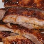 A close-up of several pieces of glazed Instant Pot barbecue ribs stacked on a plate, showcasing tender baby back ribs ready to savor.